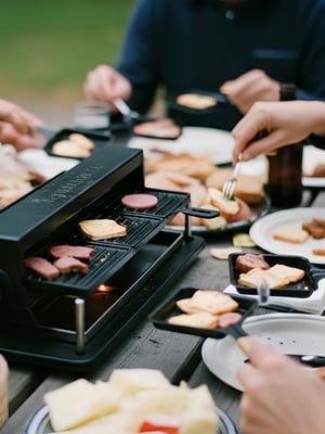 a group of people eating at a campground picnic table using a raclette as an example of RV kitchen appliances